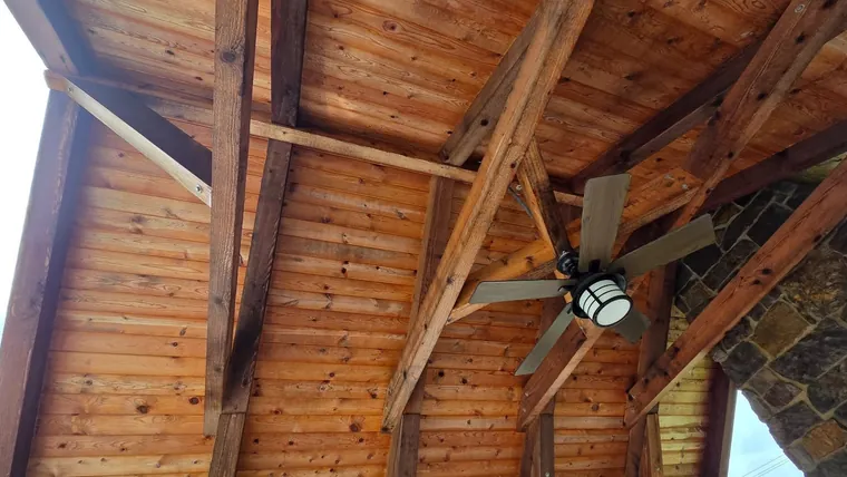 A timber pavilion ceiling after cleaning — warm cedar boards, dark exposed trusses and a ceiling fan